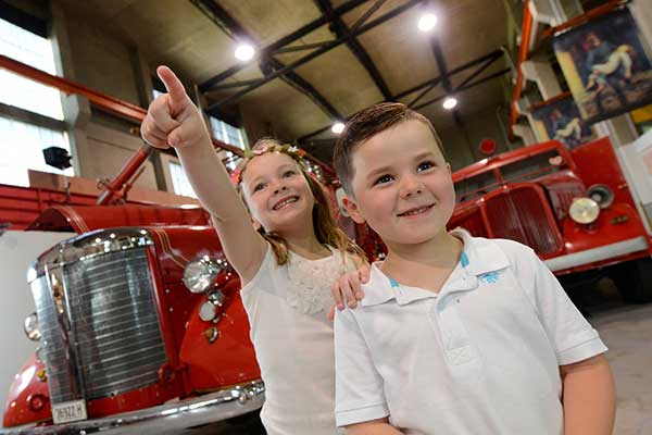 Young, excited children in front of two vintage fire trucks in a museum
