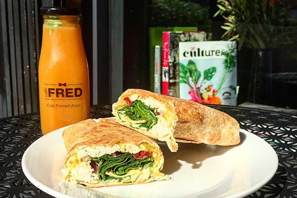 A wrap filled with greens and an omelette served on a plate with a bottle of orange juice