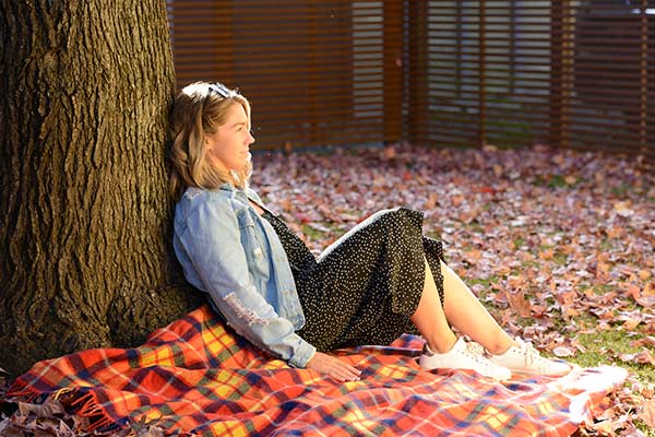 Woman relaxing against tree trunk with autumn leaves on ground