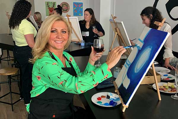 Sydney Weekender presenter smiling whilst painting and holding a wine glass