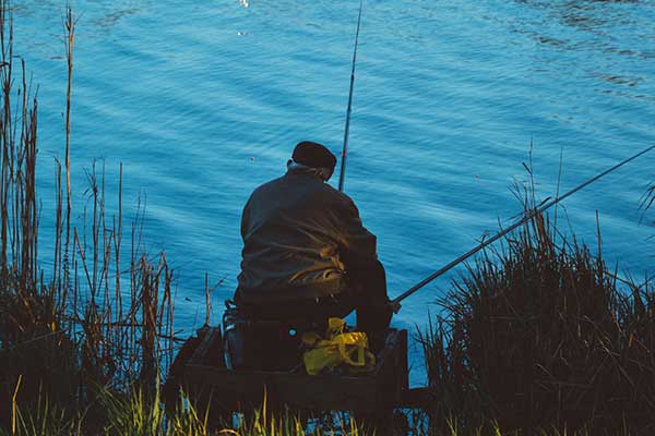 Old man sitting on edge of waterway fishing