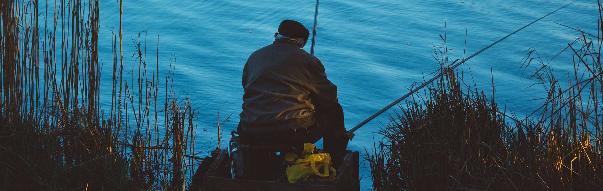 Old man sitting on edge of waterway fishing