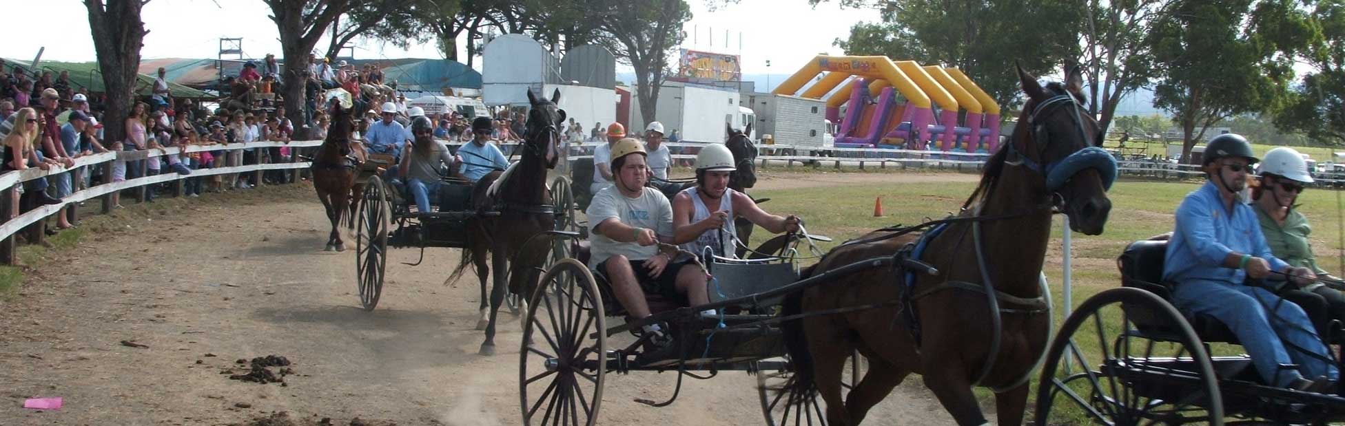 Several horse buggies racing around dirt track