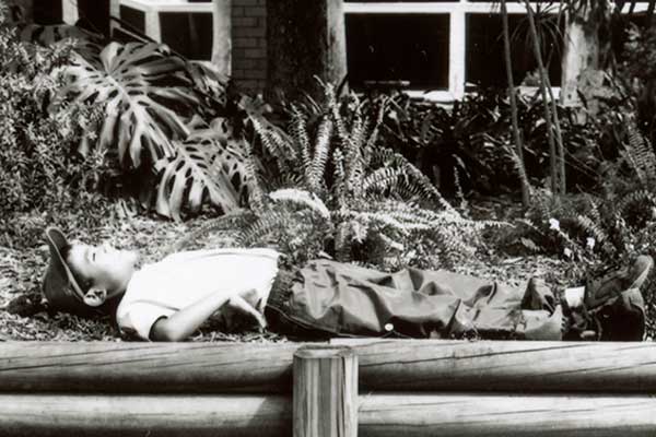 Black and white image of boy lying in garden bed on green promo background