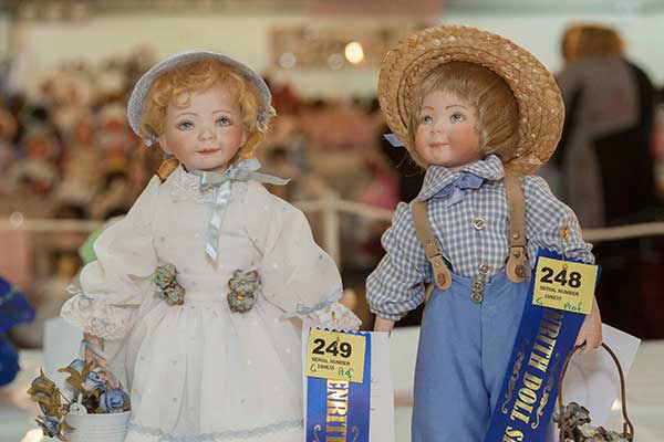 Male and female dolls on display, both with blue prize ribbons