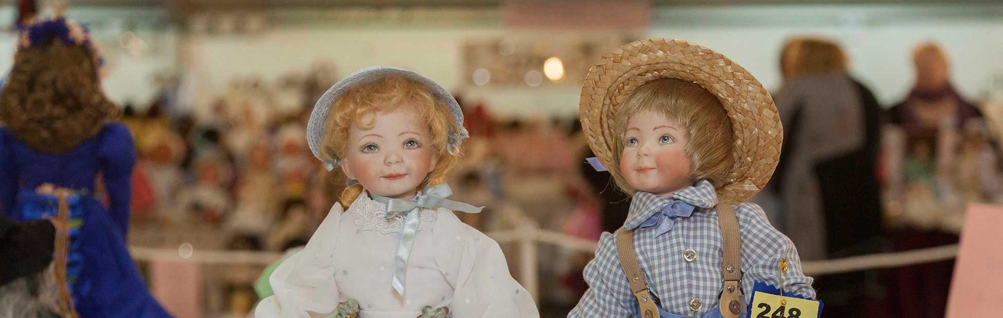 Male and female dolls on display, both with blue prize ribbons
