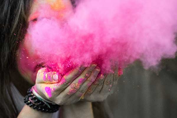 woman with long nails holding colour powder blowing it to make a cloud