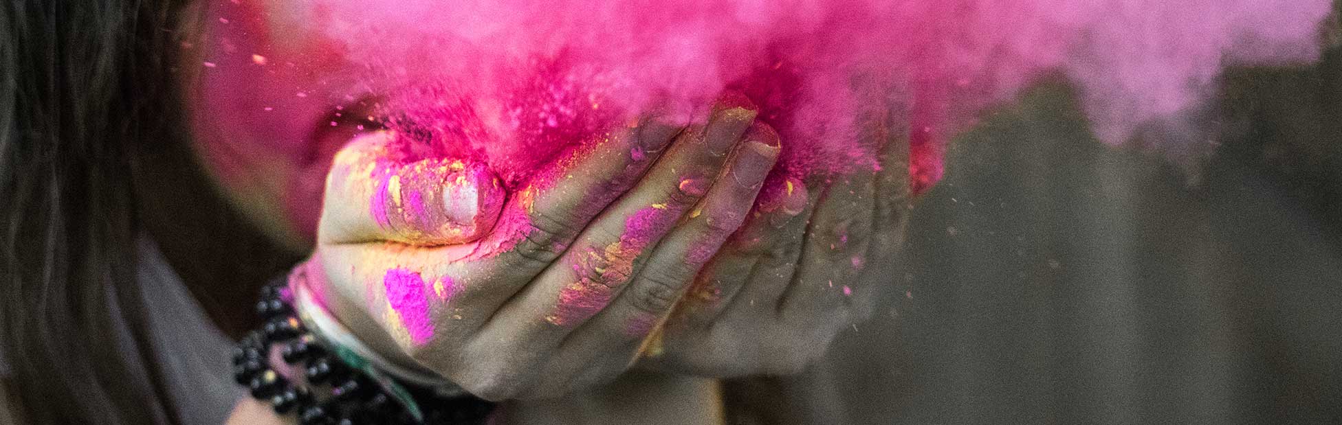 woman with long nails holding colour powder blowing it to make a cloud