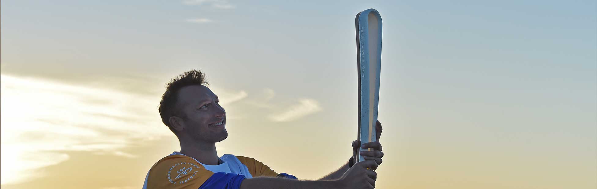 Ian Thorpe holding the Queens Baton in front of sunset sky
