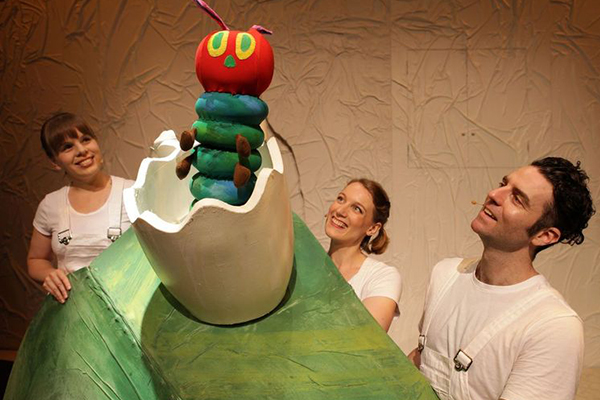 Caterpillar puppet with actors looking at it smiling