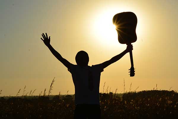Person holding up guitar against sun in field