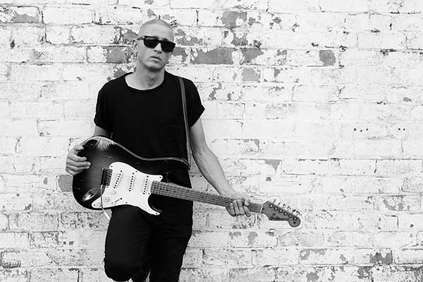 Diesel leaning on wall holding guitar