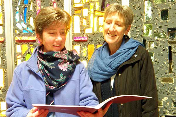 Two women holding a choir book smiling