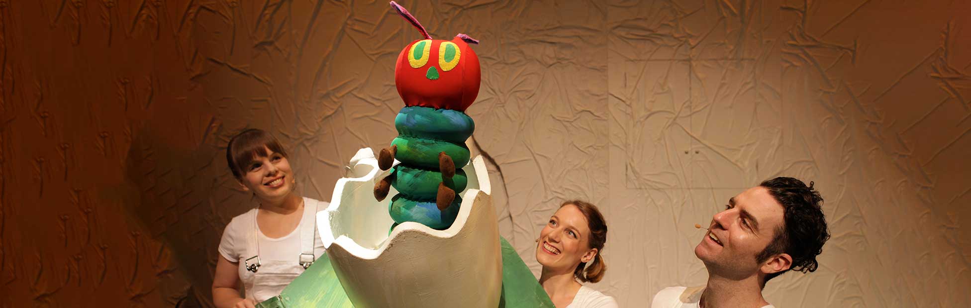 Caterpillar puppet with actors looking at it smiling