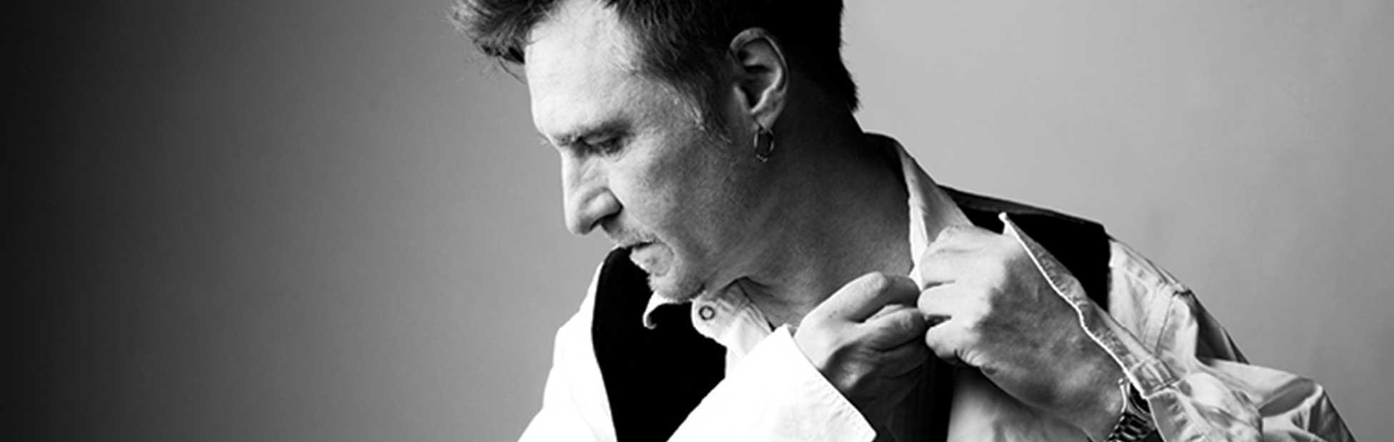 John Waite in collared shirt and vest with hand to his neck