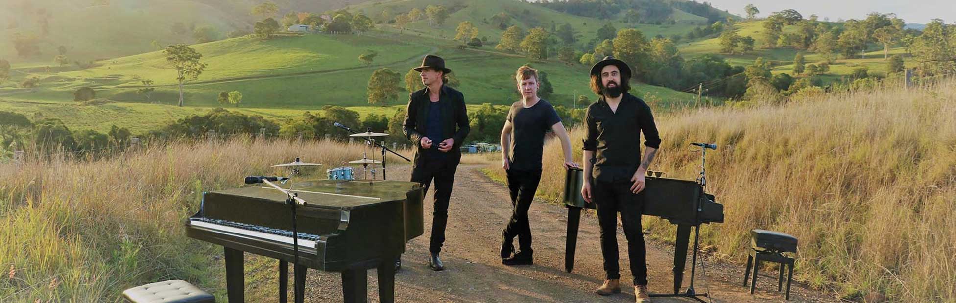 Three men in black posing on countryside dirt road with their musical instruments