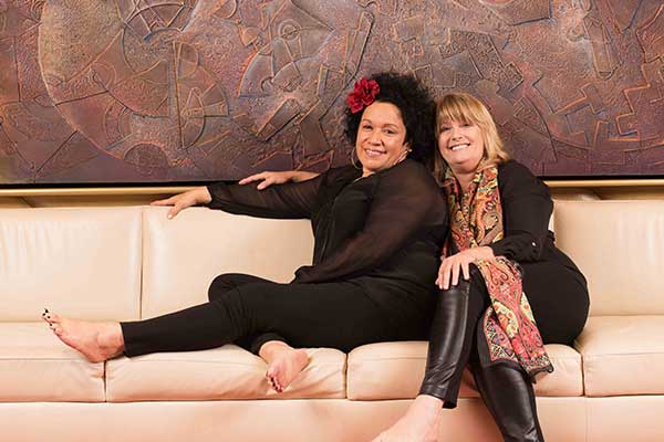 Two women sitting back to back on couch smiling