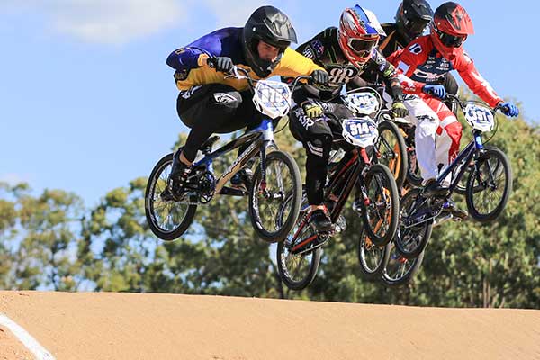 Five racing BMX riders on jump in full gear