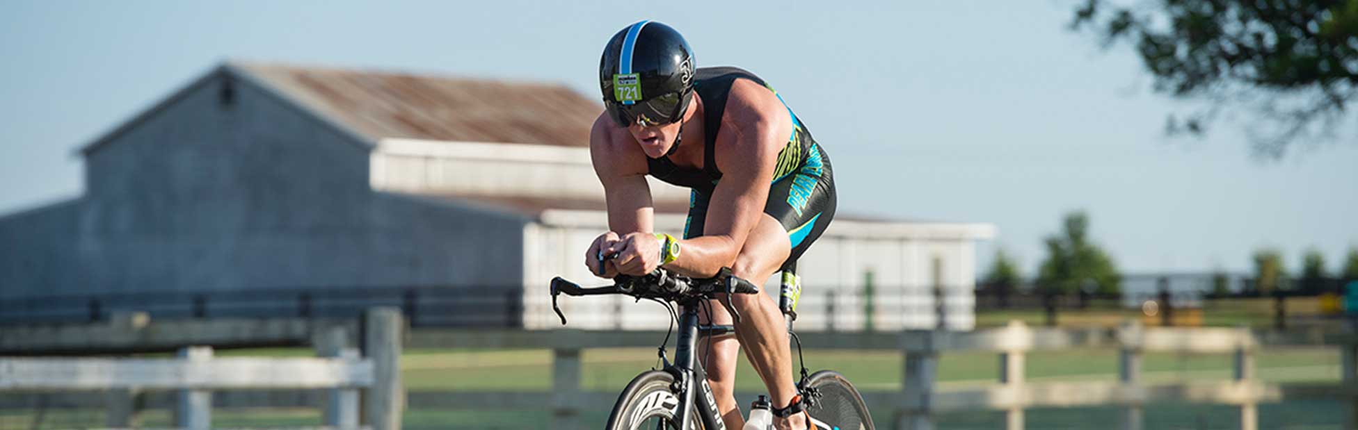 Male IRONMAN competitor on bike with shed in background
