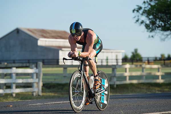Male IRONMAN competitor on bike with shed in background