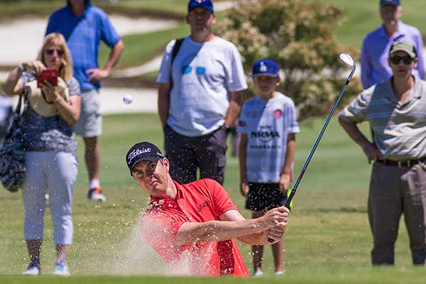 Golfer chipping onto the green making sand fly