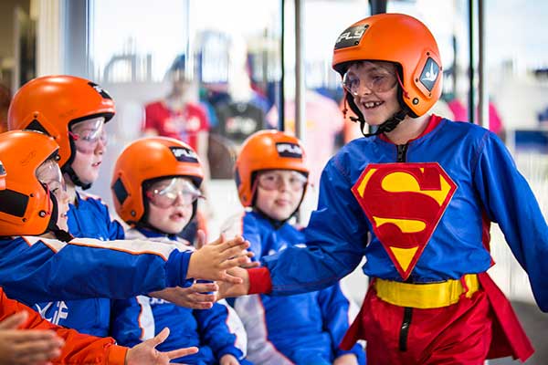 Boy dressed as superman at iFLY high fiving other children