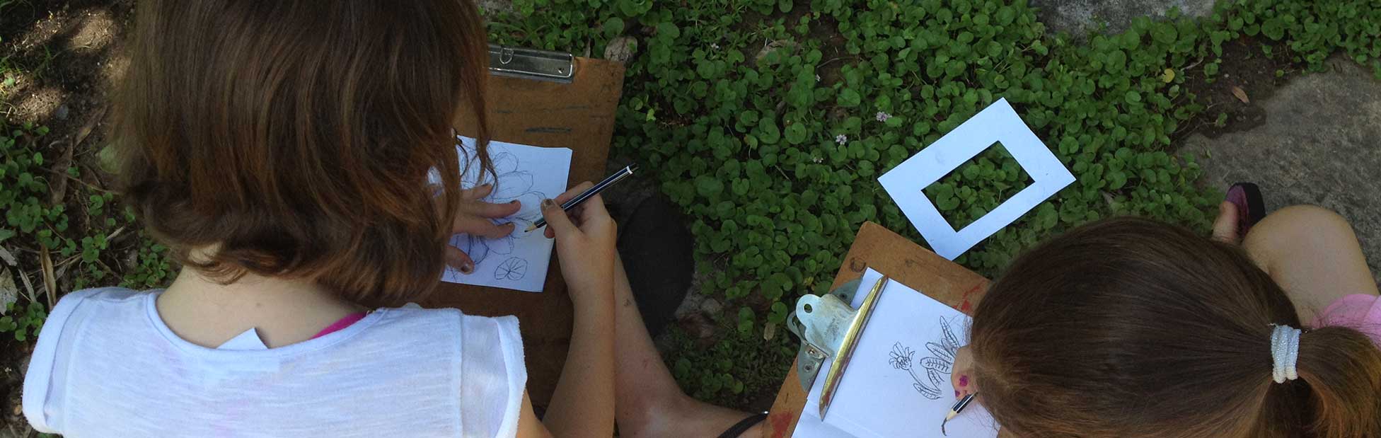 Girls in garden drawing on paper mounted on clipboards