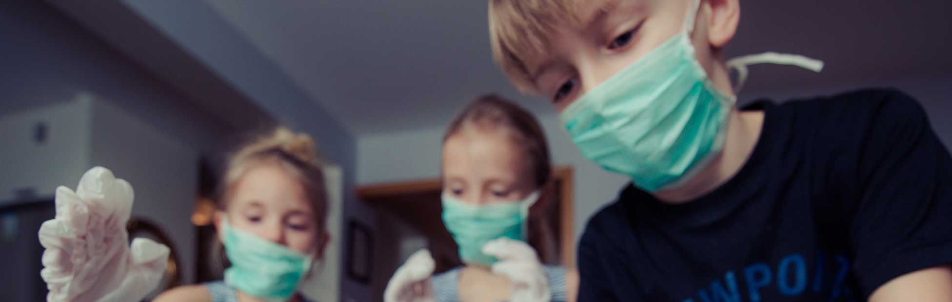 Children wearing medical masks looking a toy doll
