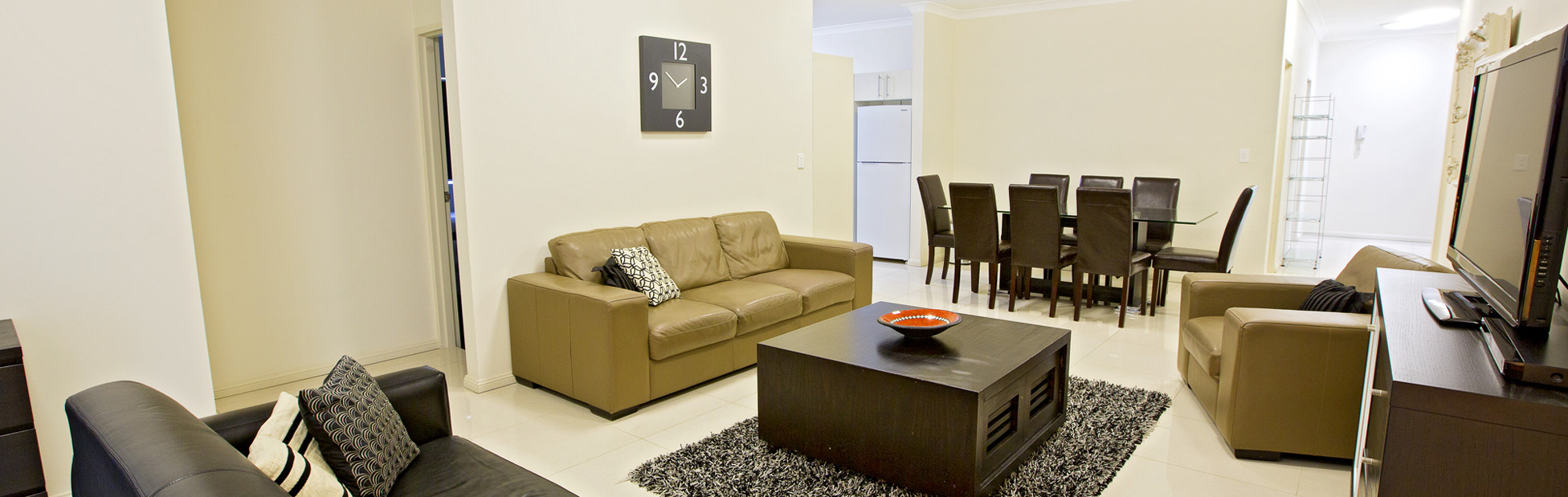 Living room with lounge, coffee table, TV on a unit and a dining table set with chairs.