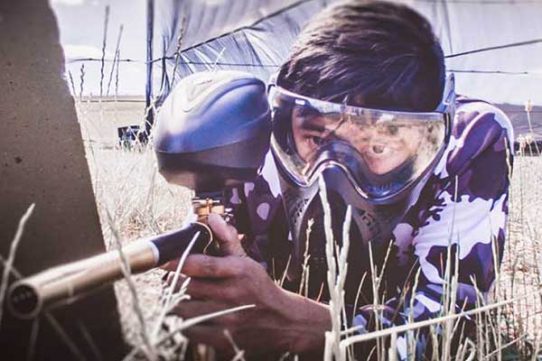 Man wearing protective face mask and camouflage gear holding a paintball gun