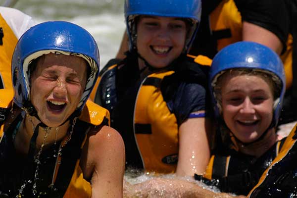 A group of young girls in a raft sailing down a wild white water river with safety gear on