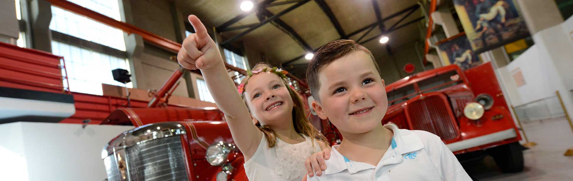 Two young kids standing in front of vintage red fire trucks