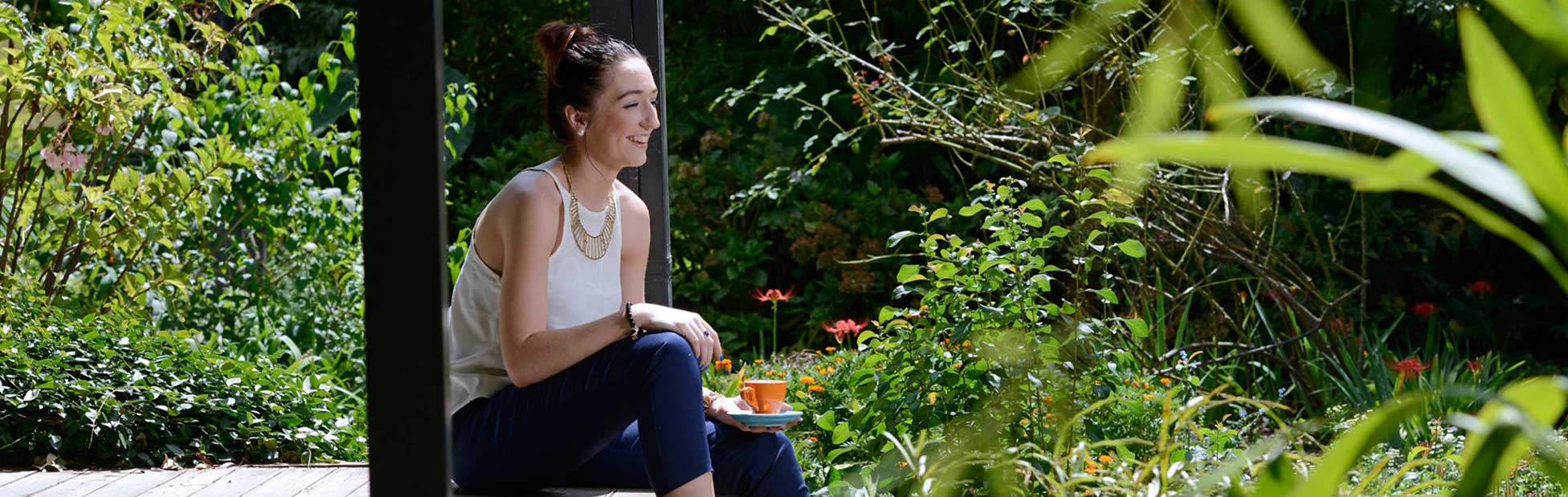 Young lady sitting on a verandah surrounded by a lucious green garden