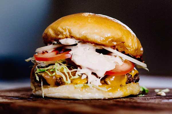 A close up of a burger with cheese, tomato and mayonaise