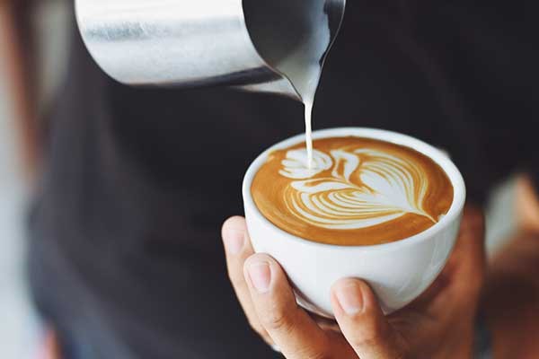 Mans hand pouring milk in decorative shape into coffee mug