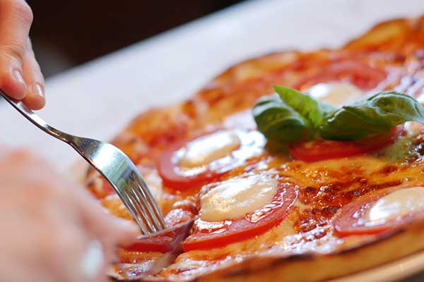 A fork and knife cutting into a pepperoni pizza