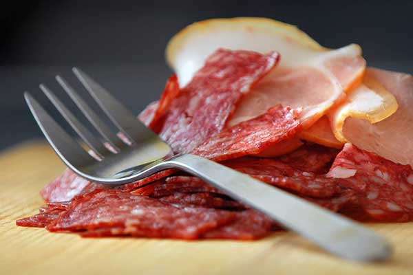 Sliced salami on wooden board with silver fork on top