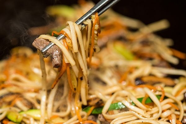 Chopsticks holding a piece of meat and noodles