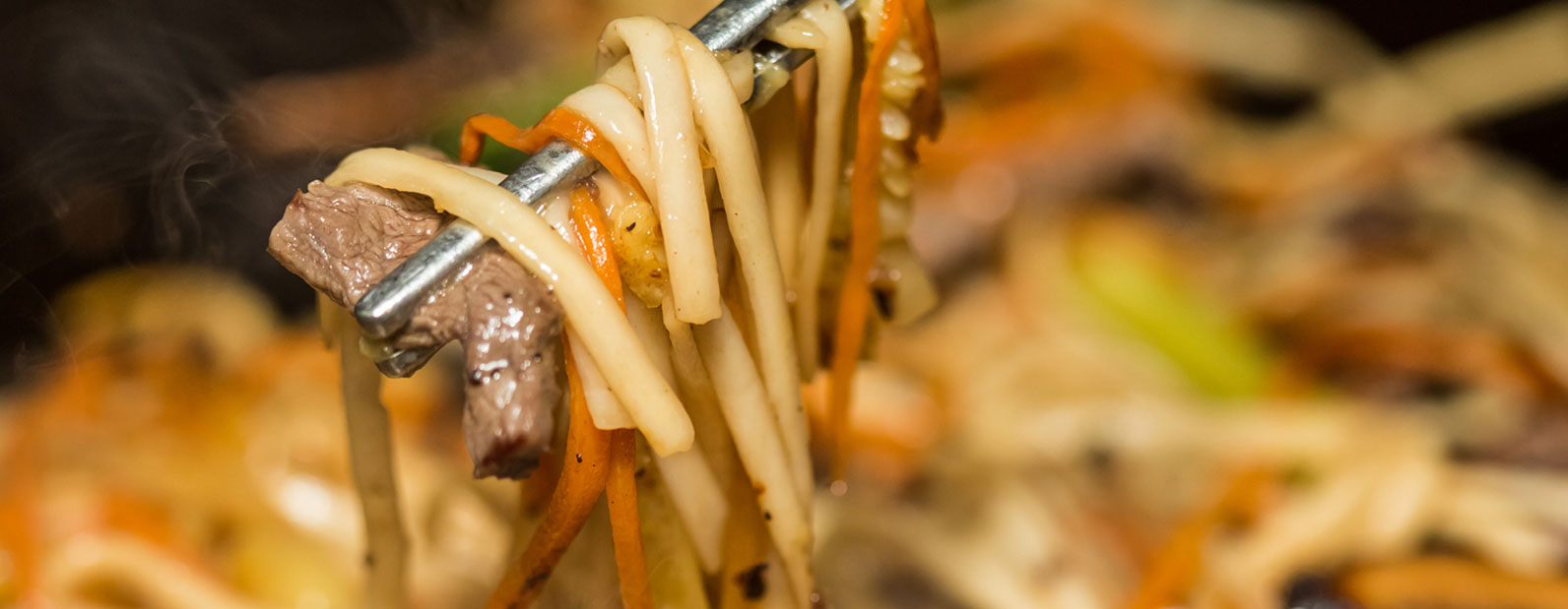 Chopsticks holding a piece of meat and noodles