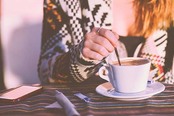 Woman sitting in sunshine stirring coffee