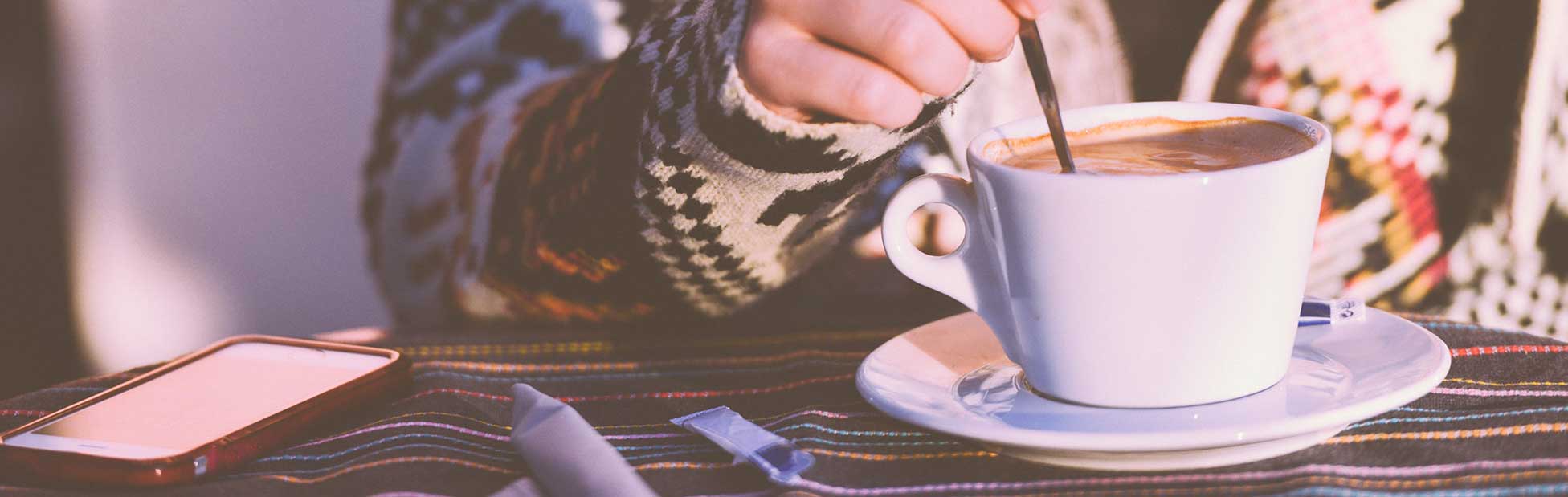 Woman sitting in sunshine stirring coffee