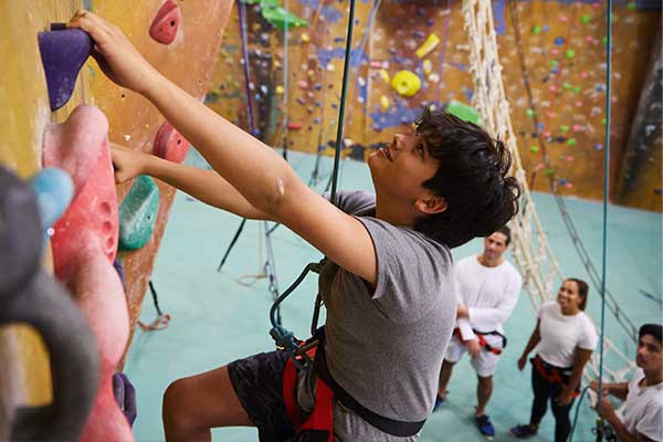 A young man with a hardness on climbing up a rock wall with family watching