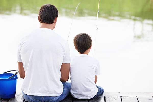 Father and son sitting on a river bank fishing