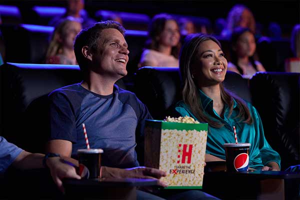 Young couple wearing glasses and eating popcorn looking up at the screen in the cinema smiling