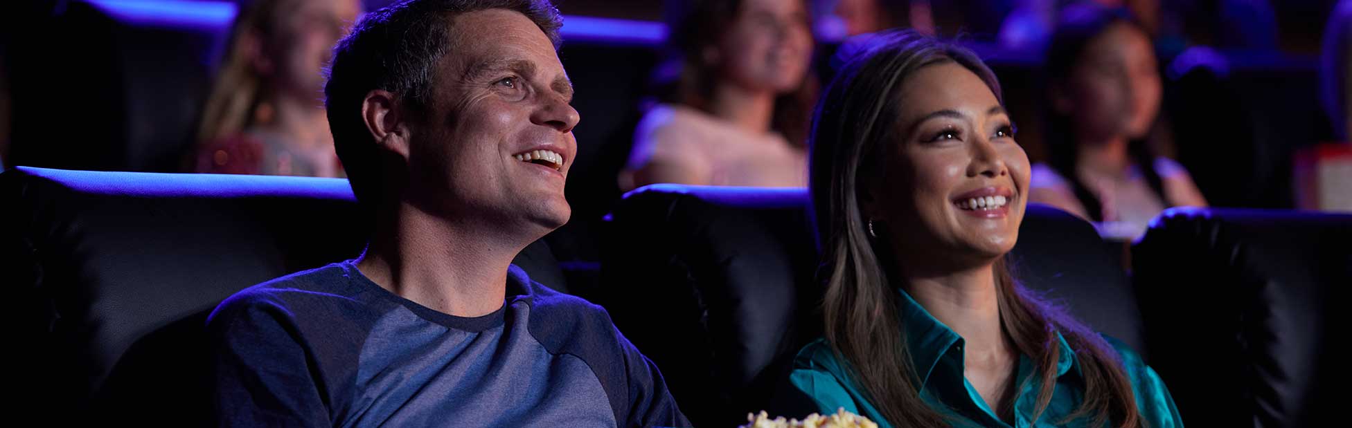 Young couple wearing glasses and eating popcorn looking up at the screen in the cinema smiling